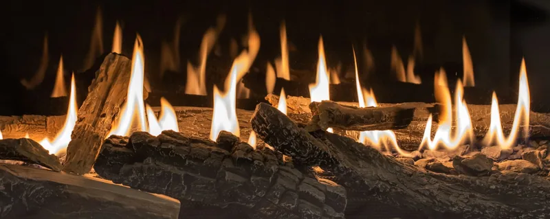 Des flammes jaillissent de bûches en céramique dans la cheminée, projetant une lumière chaude.