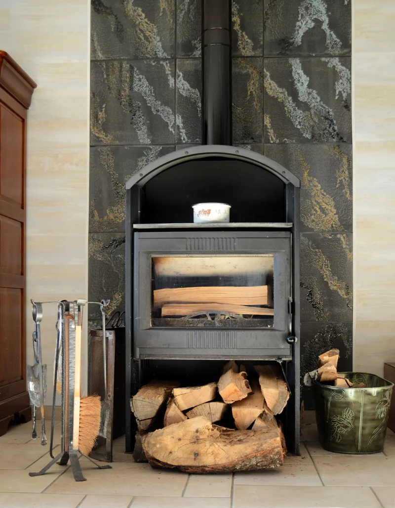 Cheminée avec bûches empilées, outils en métal et carreaux muraux décoratifs.